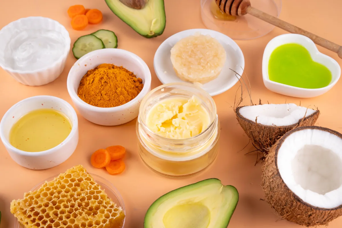 Natural skincare ingredients including turmeric, coconut, avocado, honeycomb and oils arranged on a peach background