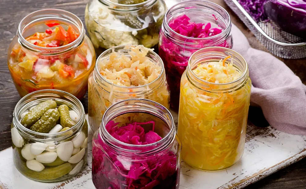 Jars of naturally fermented vegetables including sauerkraut, kimchi and pickles on a wooden board
